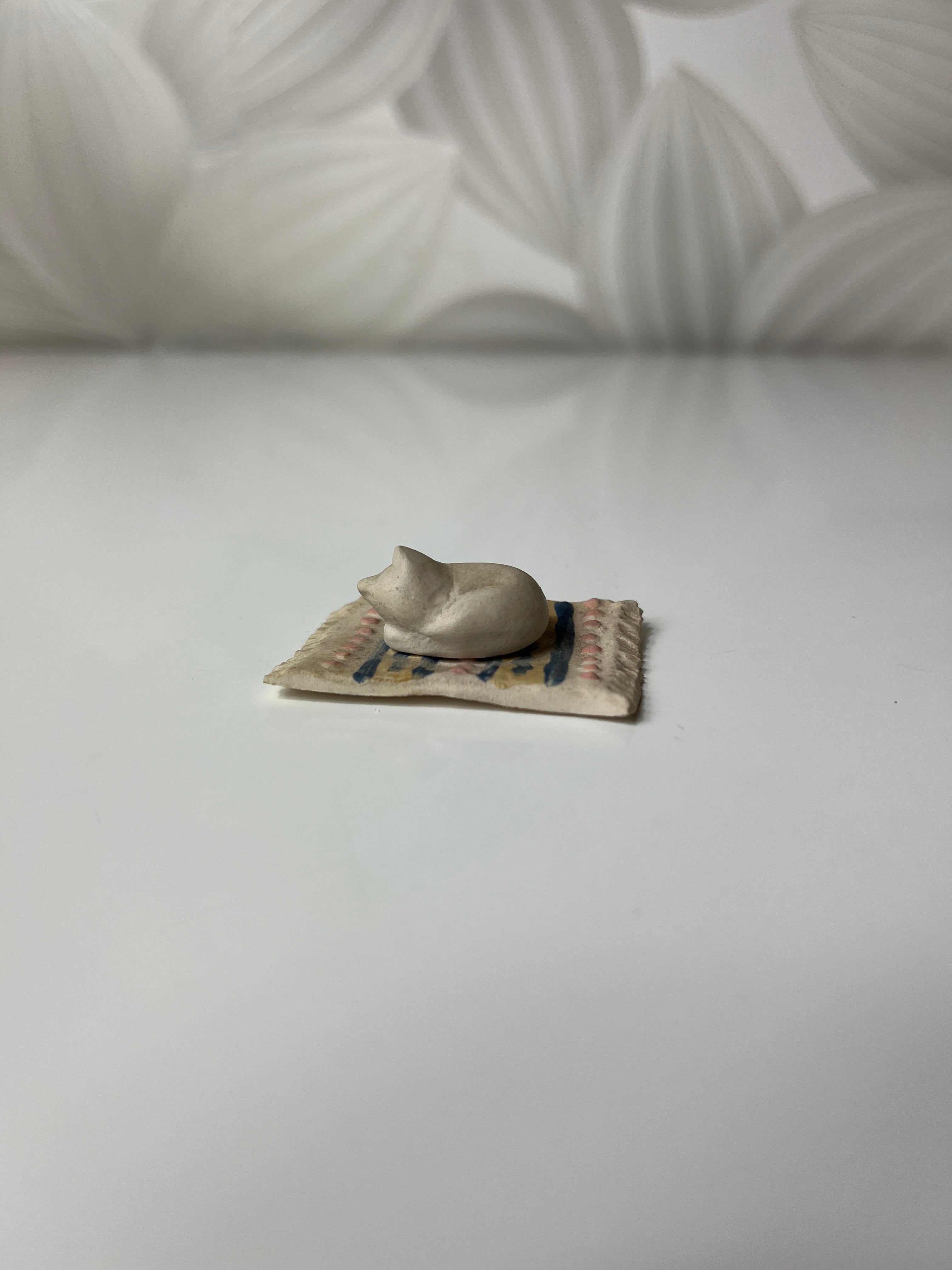 Mažas keramikinis katinas ant kilimėlio
