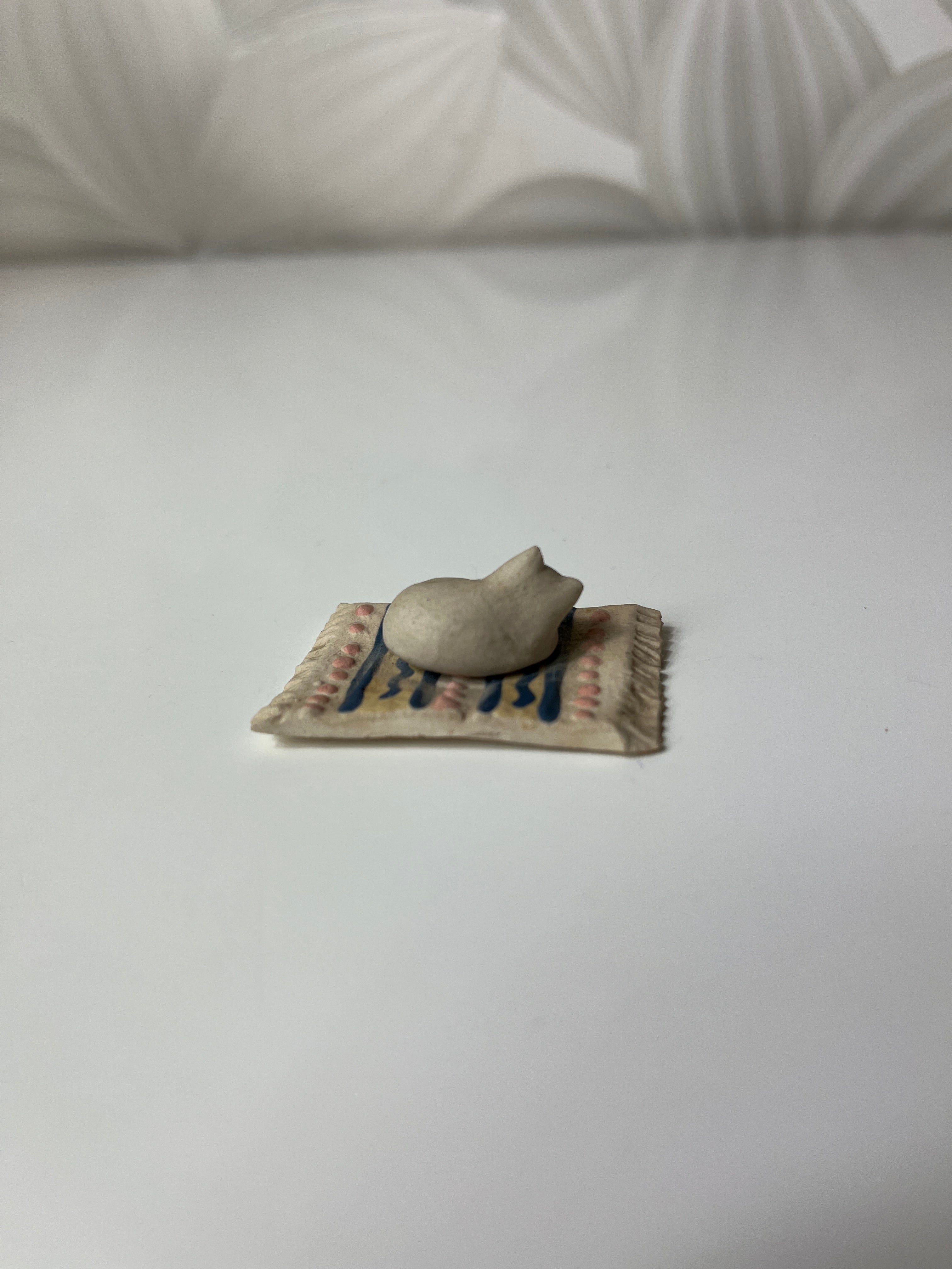 Mažas keramikinis katinas ant kilimėlio